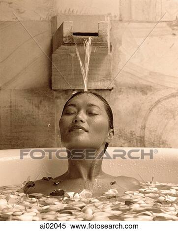 Woman relaxing in bathtub with flower petals, water pouring on head View Large Photo Image Stock Photography - Woman relaxing in bathtub with flower petals, water pouring on head. Fotosearch