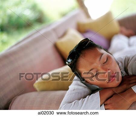 Stock Image - Woman relaxing on sofa outdoors, eyes closed. Fotosearch