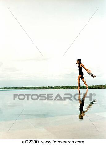 Stock Image - Woman running on water's edge with reflection.. Fotosearch