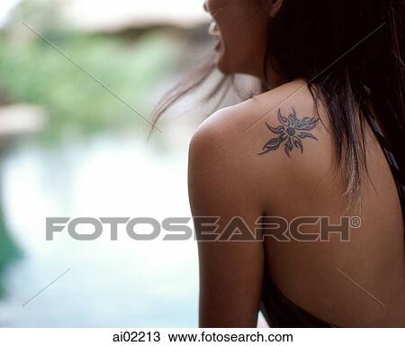Stock Image - Woman sitting by side of swimming pool, tattoo on shoulder. Fotosearch