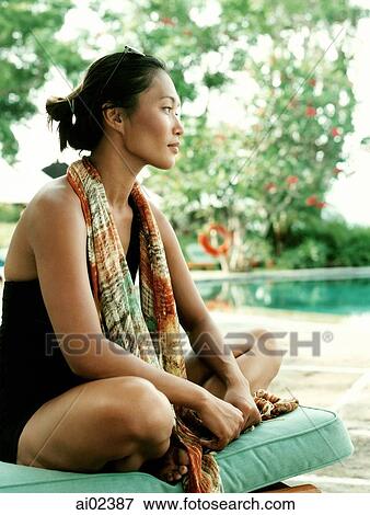 Woman sitting on deck chair looking off camera, pool in background. View Large Photo Image Stock Photo - Woman sitting on deck chair looking off camera, pool in background.. Fotosearch