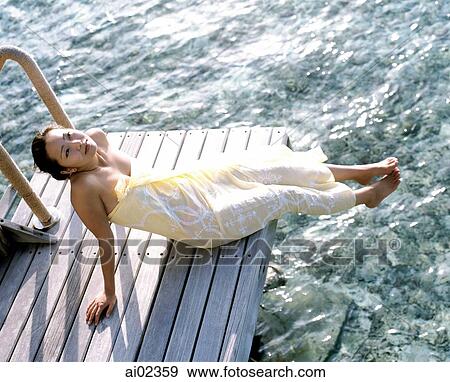 Stock Photo - Woman sitting on dock stretching, water in background, elevated position. Fotosearch