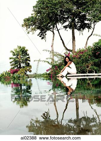 Woman sitting on water's edge with trees with reflection. View Large Photo Image Stock Photo - Woman sitting on water's edge with trees with reflection.. Fotosearch