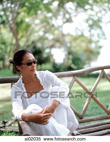 Woman sitting on wooden bench, trees behind View Large Photo Image Stock Photography - Woman sitting on wooden bench, trees behind. Fotosearch