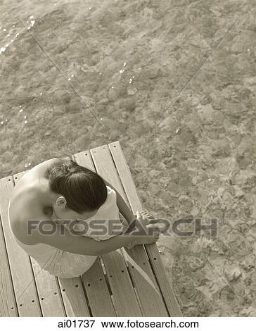 Stock Photo - Woman sitting on wooden deck with water below. Fotosearch