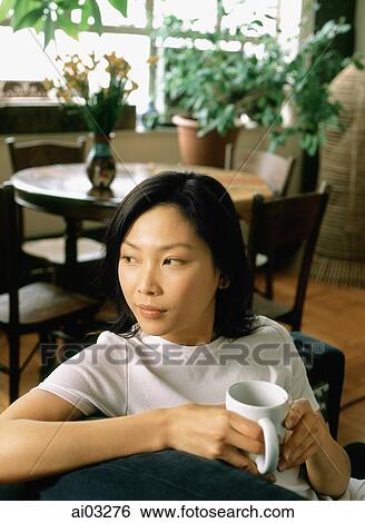 Stock Photograph - Woman sitting with a cup looking off camera. Fotosearch