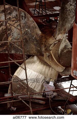 Stock Photo - Worker cleaning ship propellers at shipyard. Fotosearch