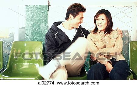 Picture - Young adult couple sitting on plastic chairs.. Fotosearch