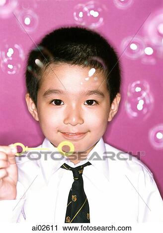 Stock Image - Young boy blowing bubbles, portrait, purple background.. Fotosearch