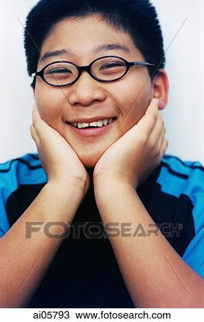 Stock Image - Young boy wearing glasses resting head on hands, laughing, portrait ( high grain). Fotosearch