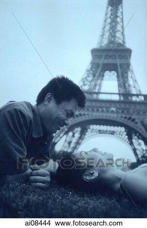 Picture - Young couple lying on grass, Eiffel Tower in background.. Fotosearch