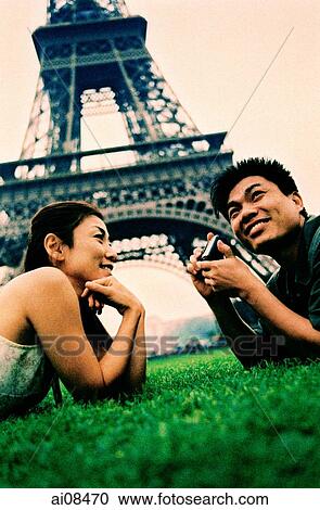 Young couple lying on grass, holding camera, Eiffel Tower in background. (high-grained) View Large Photo Image Stock Image - Young couple lying on grass, holding camera, Eiffel Tower in background. (high-grained). Fotosearch