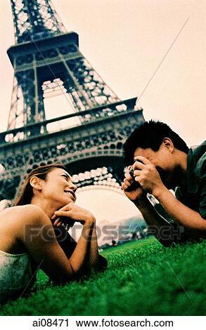 Young couple lying on grass, young woman posing for camera, smiling, Eiffel Tower in background. (high-grained) View Large Photo Image Stock Image - Young couple lying on grass, young woman posing for camera, smiling, Eiffel Tower in background. (high-grained). Fotosearch
