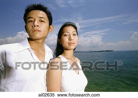 Young couple standing on beach, blue sky and beach in background, portrait View Large Photo Image Stock Photography - Young couple standing on beach, blue sky and beach in background, portrait. Fotosearch