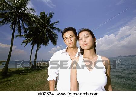 Young couple standing on beach, coconut trees in background, portrait View Large Photo Image Picture - Young couple standing on beach, coconut trees in background, portrait. Fotosearch