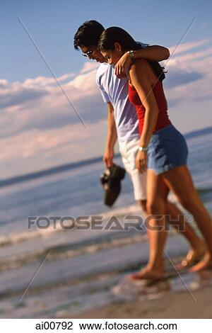 Young couple walking on beach, man with arm around woman's shoulder View Large Photo Image Stock Image - Young couple walking on beach, man with arm around woman's shoulder. Fotosearch