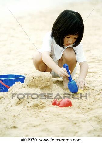 Stock Image - Young girl playing in sand with toy pail and spade. Fotosearch