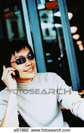 Stock Image - Young man, causal dress, wearing sunglasses using cellular phone ( high grain). Fotosearch
