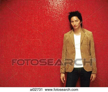 Stock Image - Young man in brown jacket leaning against orange/red background.. Fotosearch