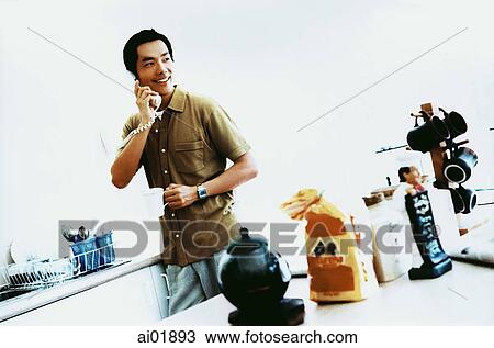 Young man in kitchen, holding cup, using telephone, looking off camera ( high grain) View Large Photo Image Stock Image - Young man in kitchen, holding cup, using telephone, looking off camera ( high grain). Fotosearch