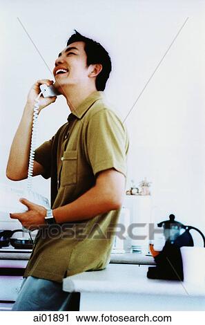 Young man leaning on kitchen counter using telephone, laughing ( high grain) View Large Photo Image Stock Image - Young man leaning on kitchen counter using telephone, laughing ( high grain). Fotosearch