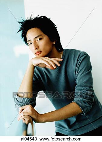 Stock Image - Young man leaning on rail, hand on chin. Fotosearch
