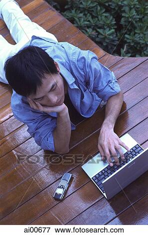 Young man lying on floor, using laptop View Large Photo Image Stock Photo - Young man lying on floor, using laptop. Fotosearch