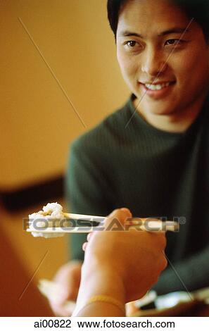 Young man smiling, hand holding chopstick with sushi in foreground View Large Photo Image Stock Image - Young man smiling, hand holding chopstick with sushi in foreground. Fotosearch