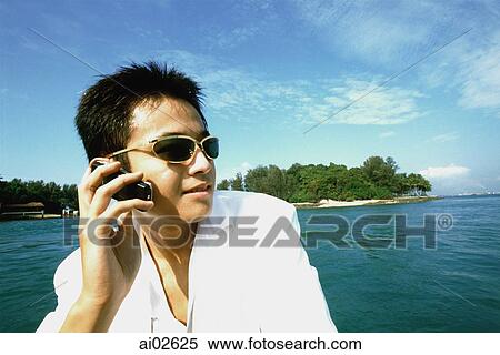 Young man with sunglasses using cellular phone, blue sky and water in background View Large Photo Image Stock Photography - Young man with sunglasses using cellular phone, blue sky and water in background. Fotosearch