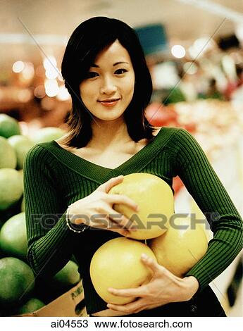 Stock Image - Young woman holding fruit, portrait.. Fotosearch