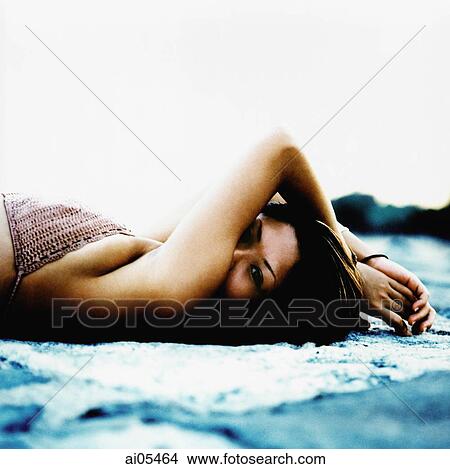 Young woman lying wearing bikini lying down on beach, face partially concealed by arm View Large Photo Image Picture - Young woman lying wearing bikini lying down on beach, face partially concealed by arm. Fotosearch