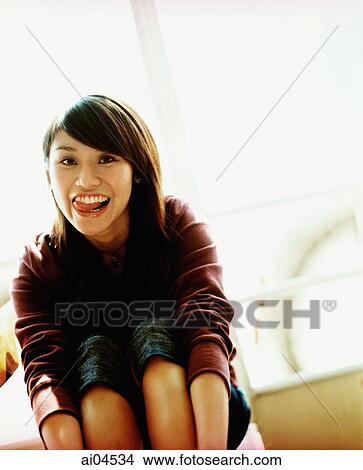 Young woman sitting, smiling and sticking out tongue, portrait. View Large Photo Image Picture - Young woman sitting, smiling and sticking out tongue, portrait.. Fotosearch
