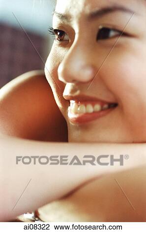 Stock Image - Young woman smiling, resting head on arms.. Fotosearch