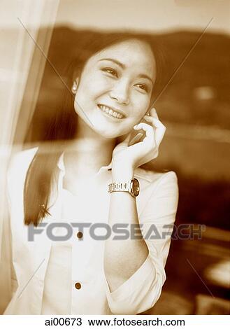 Young woman standing behind window, talking on cellular phone View Large Photo Image Stock Image - Young woman standing behind window, talking on cellular phone. Fotosearch