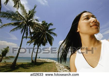 Young woman standing on beach, looking up, coconut trees in background, low angle view View Large Photo Image Stock Image - Young woman standing on beach, looking up, coconut trees in background, low angle view. Fotosearch