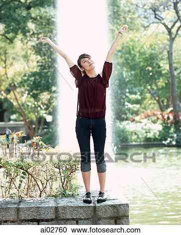 Young woman standing with arms outstretched, fountain in background. View Large Photo Image Stock Image - Young woman standing with arms outstretched, fountain in background.. Fotosearch