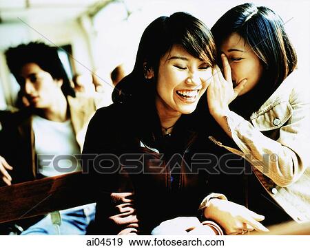 Stock Photo - Young woman whispering to laughing friend, man in background. Fotosearch