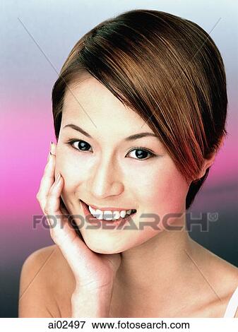 Stock Photo - Young woman with hand on chin, smiling, portrait. Fotosearch