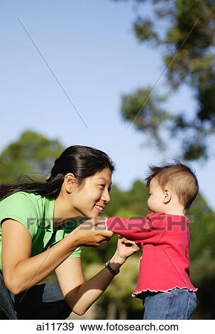 Stock Photo - Baby girl standing, mother holding her up. Fotosearch