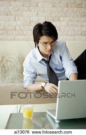 Businessman using laptop, lying on sofa View Large Photo Image Stock Photograph - Businessman using laptop, lying on sofa. Fotosearch