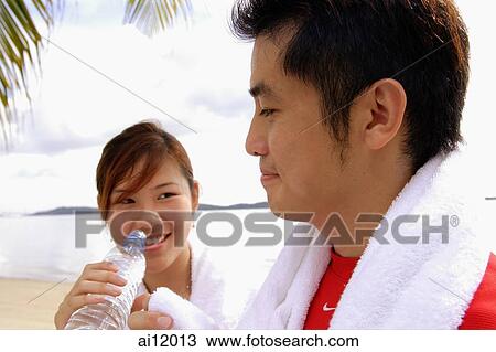 Couple at beach, woman holding water bottle, man holding towel View Large Photo Image Stock Image - Couple at beach, woman holding water bottle, man holding towel. Fotosearch
