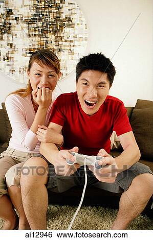 Stock Photograph - Couple at home, man holding game controller. Fotosearch