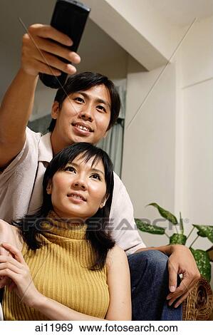 Couple at home, man holding remote control View Large Photo Image Stock Photo - Couple at home, man holding remote control. Fotosearch