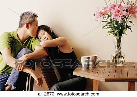 Stock Image - Couple at home, man kissing woman on the forehead. Fotosearch