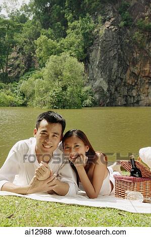 Couple by a lake, with picnic basket, looking at camera View Large Photo Image Stock Photo - Couple by a lake, with picnic basket, looking at camera. Fotosearch
