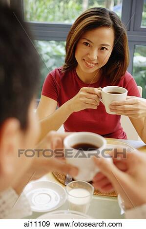 Stock Photo - Couple facing each other, holding cups of coffee. Fotosearch