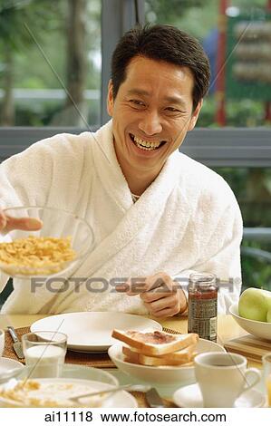 Stock Photo - Couple having breakfast, man offering bowl of cereal. Fotosearch