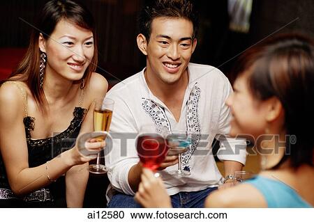 Stock Image - Couple holding drinks, facing another young woman. Fotosearch