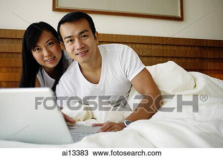 Couple in bed with laptop, looking at camera View Large Photo Image Stock Image - Couple in bed with laptop, looking at camera. Fotosearch