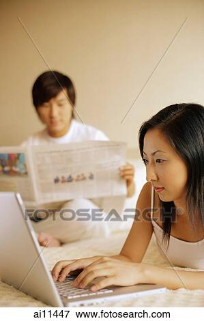 Couple in bedroom, man reading newspaper, woman using laptop View Large Photo Image Stock Photo - Couple in bedroom, man reading newspaper, woman using laptop. Fotosearch